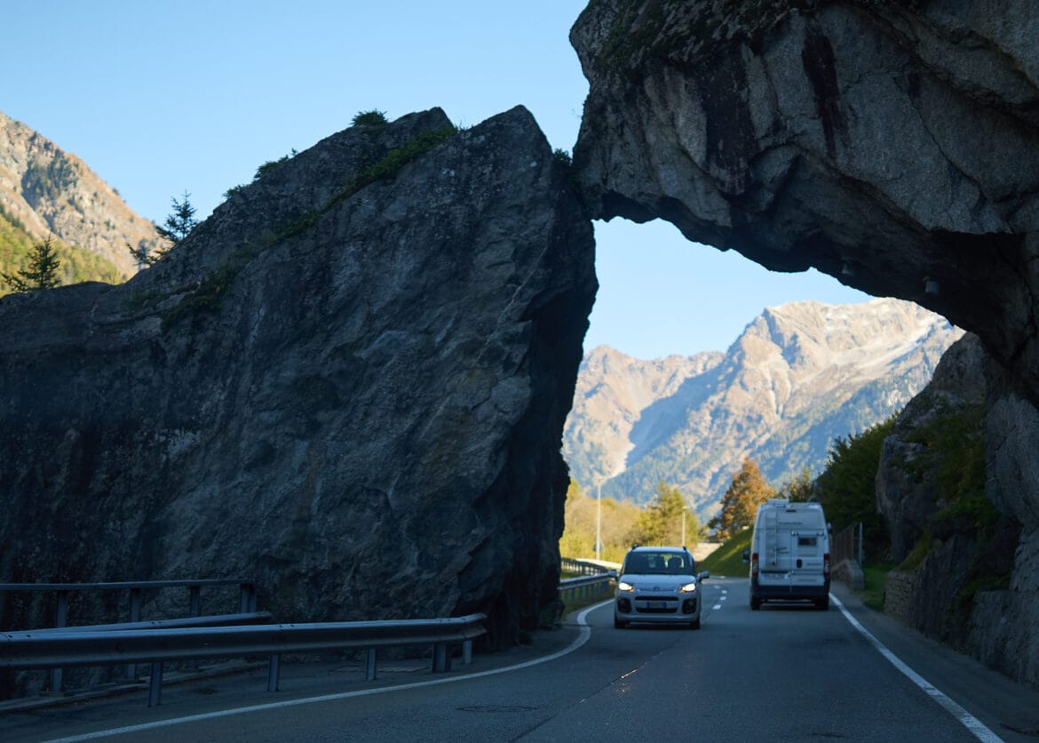 Scenic mountain road near St. Moritz passing through a rock arch with cars and Alps in background